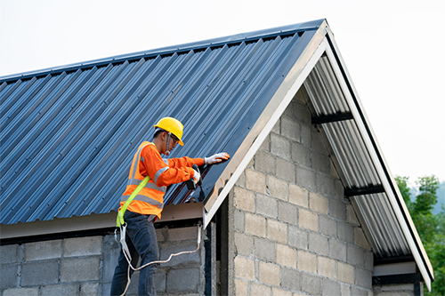 A worker in an orange safety vest is performing repairs on a house roof, highlighting construction safety practices.