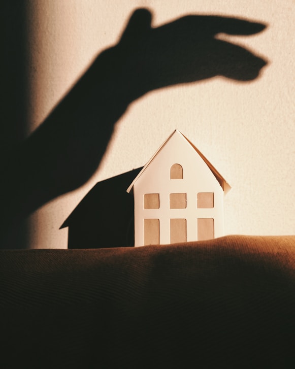 Shadow of a hand reaching over a small model house